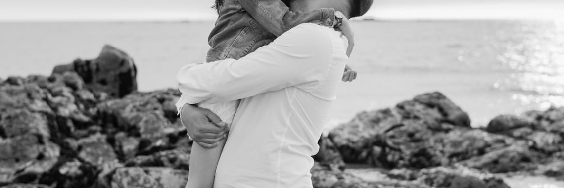 Father joyfully holds his daughter by the sea.